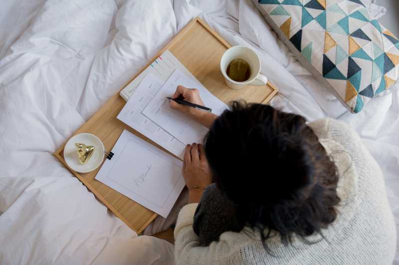 Person writing on white paper beside white ceramic mug on white textile | Photo by Paico Oficial on Unsplash